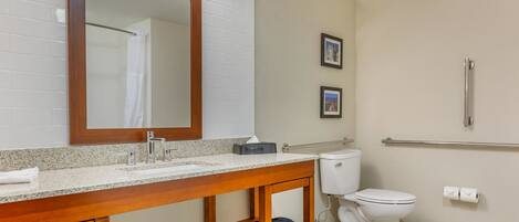 Une salle de bain avec un meuble-lavabo en bois, des toilettes blanches, une barre d’appui et deux tableaux encadrés au mur.