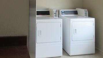 Two white front-loading washers in a corner with a dark floor and light walls.