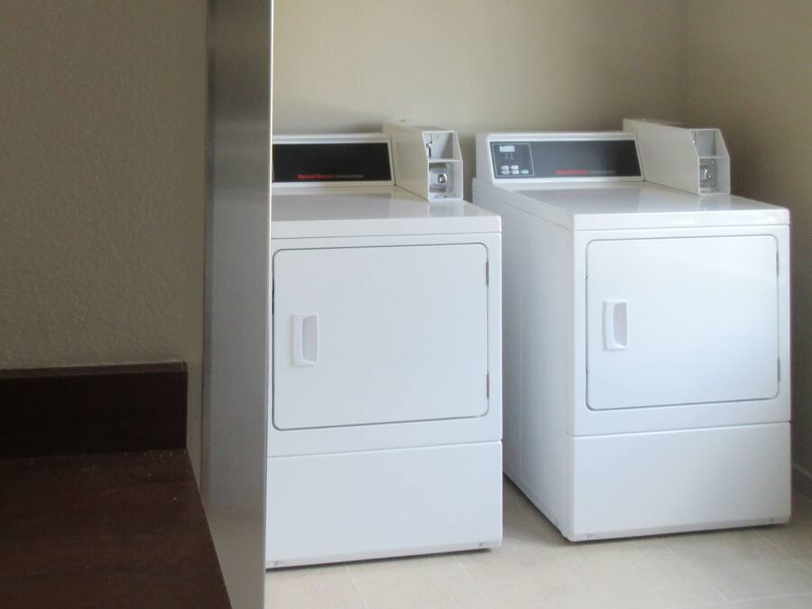 Two white front-loading washers in a corner with a dark floor and light walls.