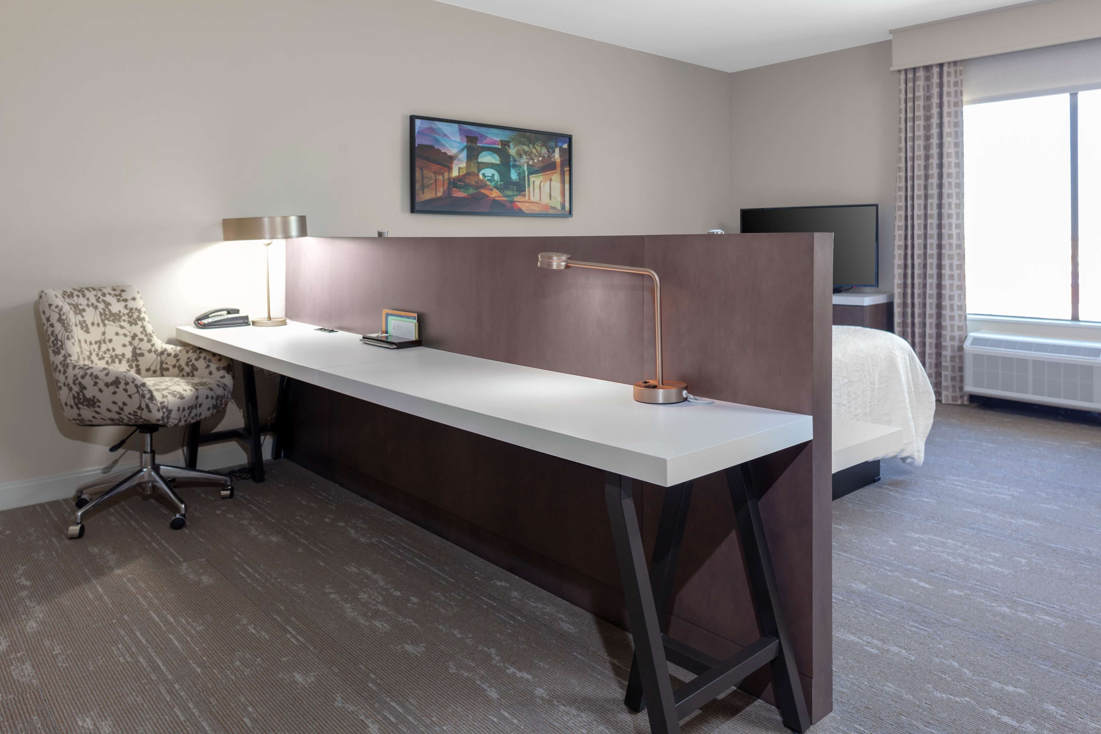A hotel room with a desk, chair, and a bed.