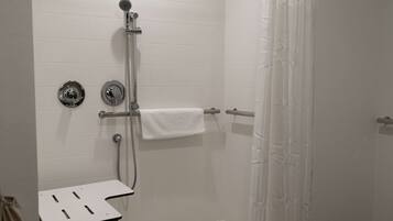 A shower area with a white tiled wall, a handheld showerhead, a towel rack, and a small table.
