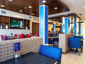 A modern restaurant with booths and tables, a TV screen, and a Christmas tree. - Holiday Inn Express & Suites Oklahoma City Airport by IHG (Oklahoma City)