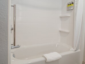 Uma banheira branca com toalha, acessórios cromados e um prateleira com produtos de higiene pessoal.