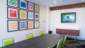 A conference room with a long table, green chairs, framed artwork on the wall, a television screen, and a carpeted floor. - Holiday Inn Express & Suites Oklahoma City Airport by IHG (Oklahoma City)