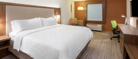 A hotel room with a large bed, a desk with a chair, a TV, and a wall-mounted air conditioner.