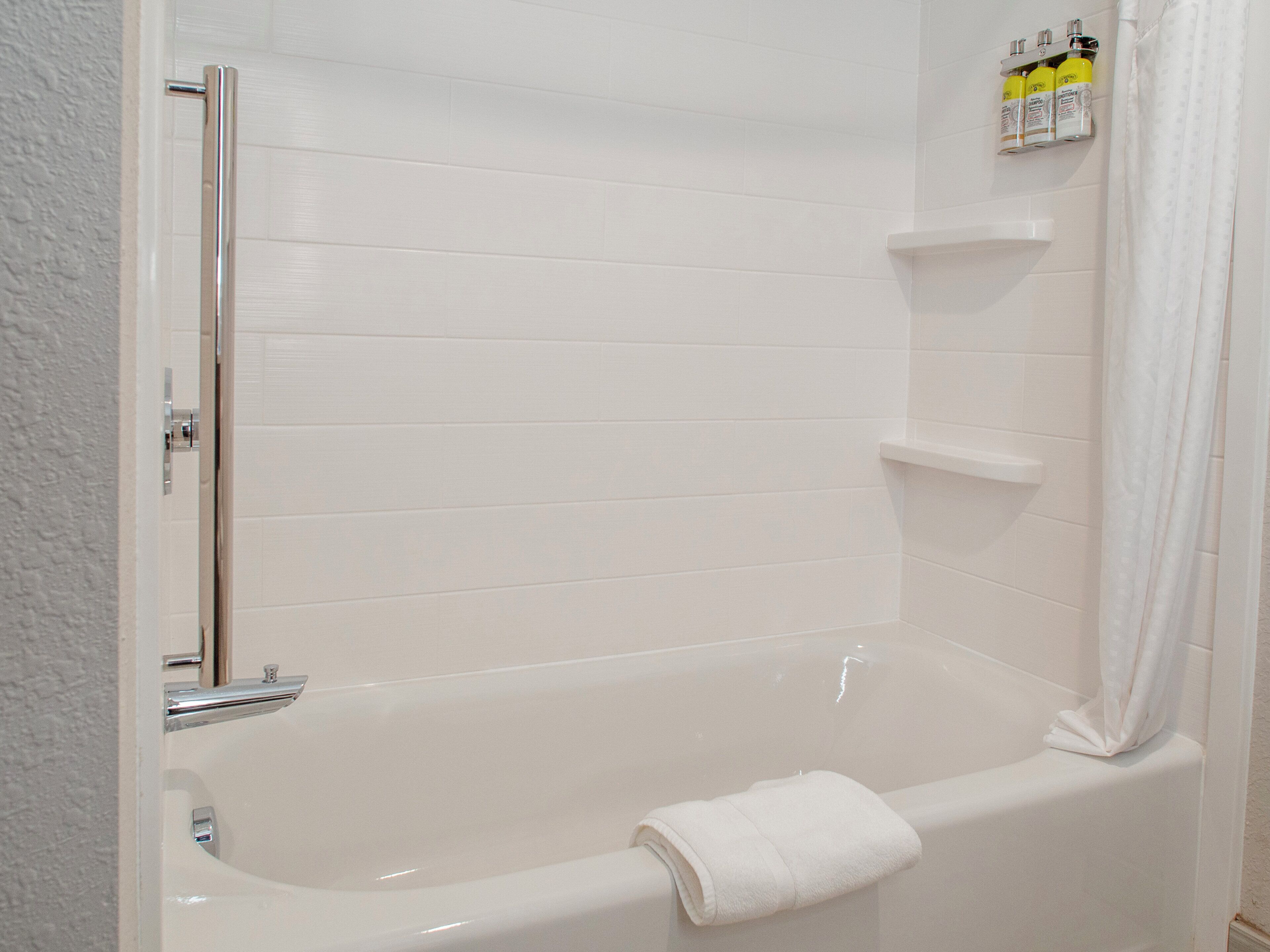 A bathroom with a bathtub, a shower curtain, and a shelf with toiletries.