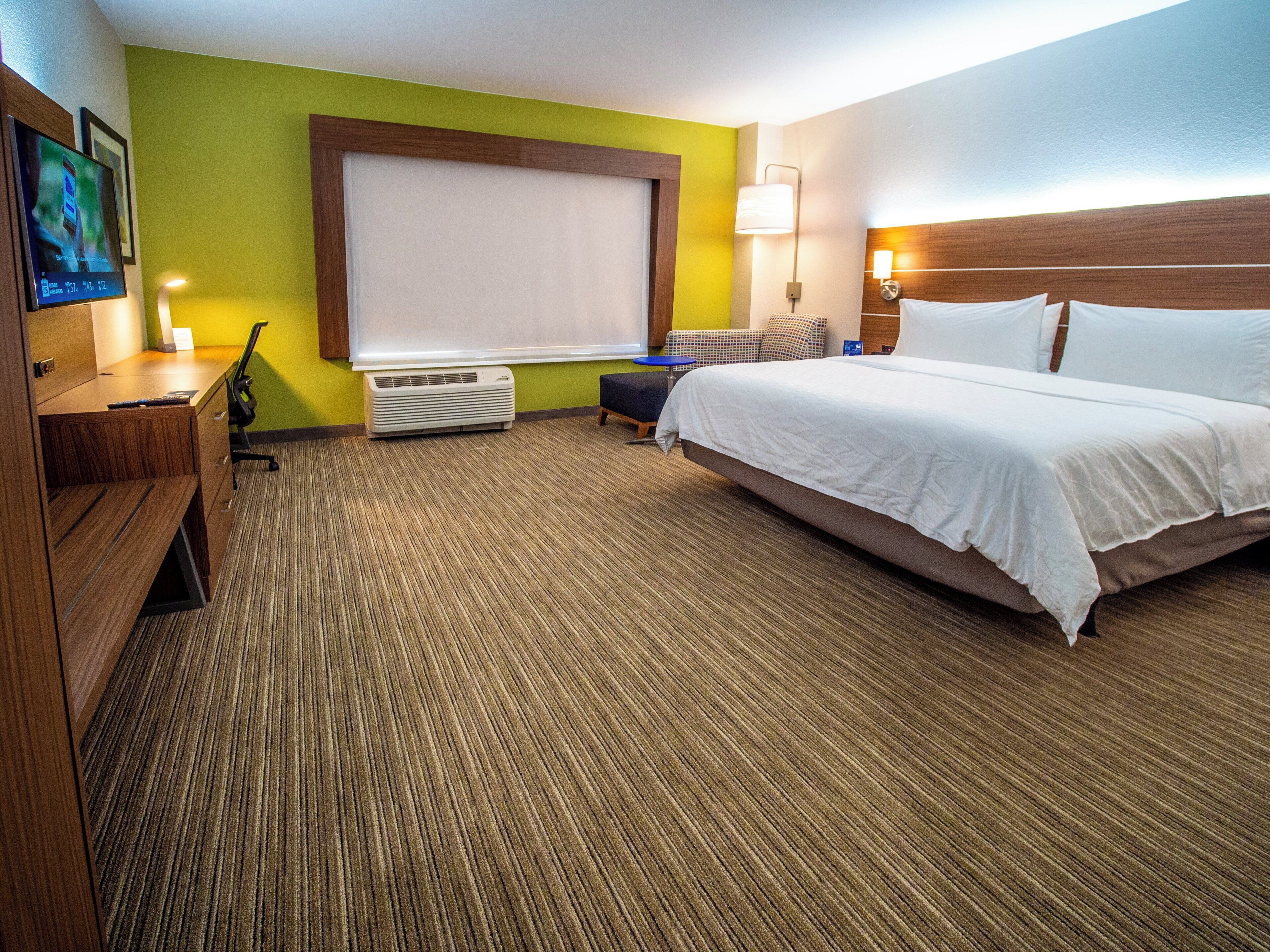 Une chambre d’hôtel avec un lit, un bureau, une chaise et une grande fenêtre.