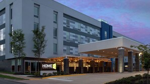 Un hotel moderno con estructura de dos pisos, entrada techada y un letrero que dice 'HOME 2 Suites by Hilton'.