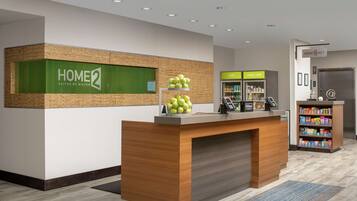 A reception desk with a green sign, a fruit display, a vending machine, and a vending area with snacks.