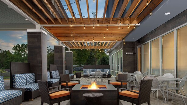 Un patio al aire libre con una chimenea, muebles de mimbre y una pérgola con luces colgantes.