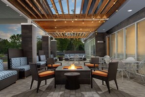 An outdoor patio with a fire pit, wicker furniture, and a pergola with string lights. - Home2 Suites by Hilton Charlottesville Downtown (Charlottesville)