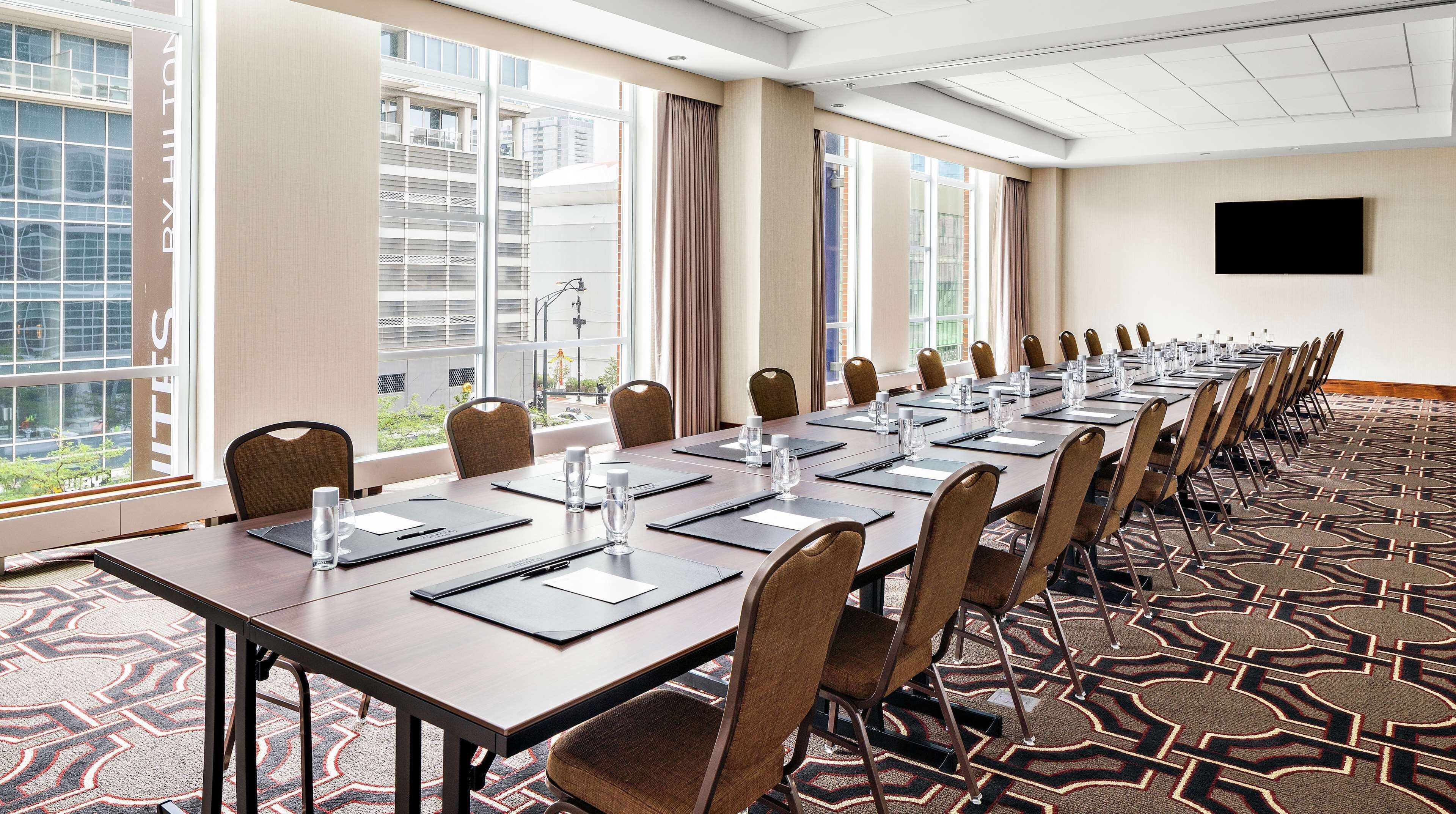 A conference room with a long table, chairs, and a TV on the wall.