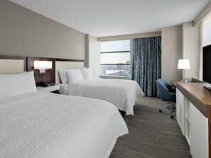 A hotel room with two beds, a desk, a chair, a TV, and a window with curtains.