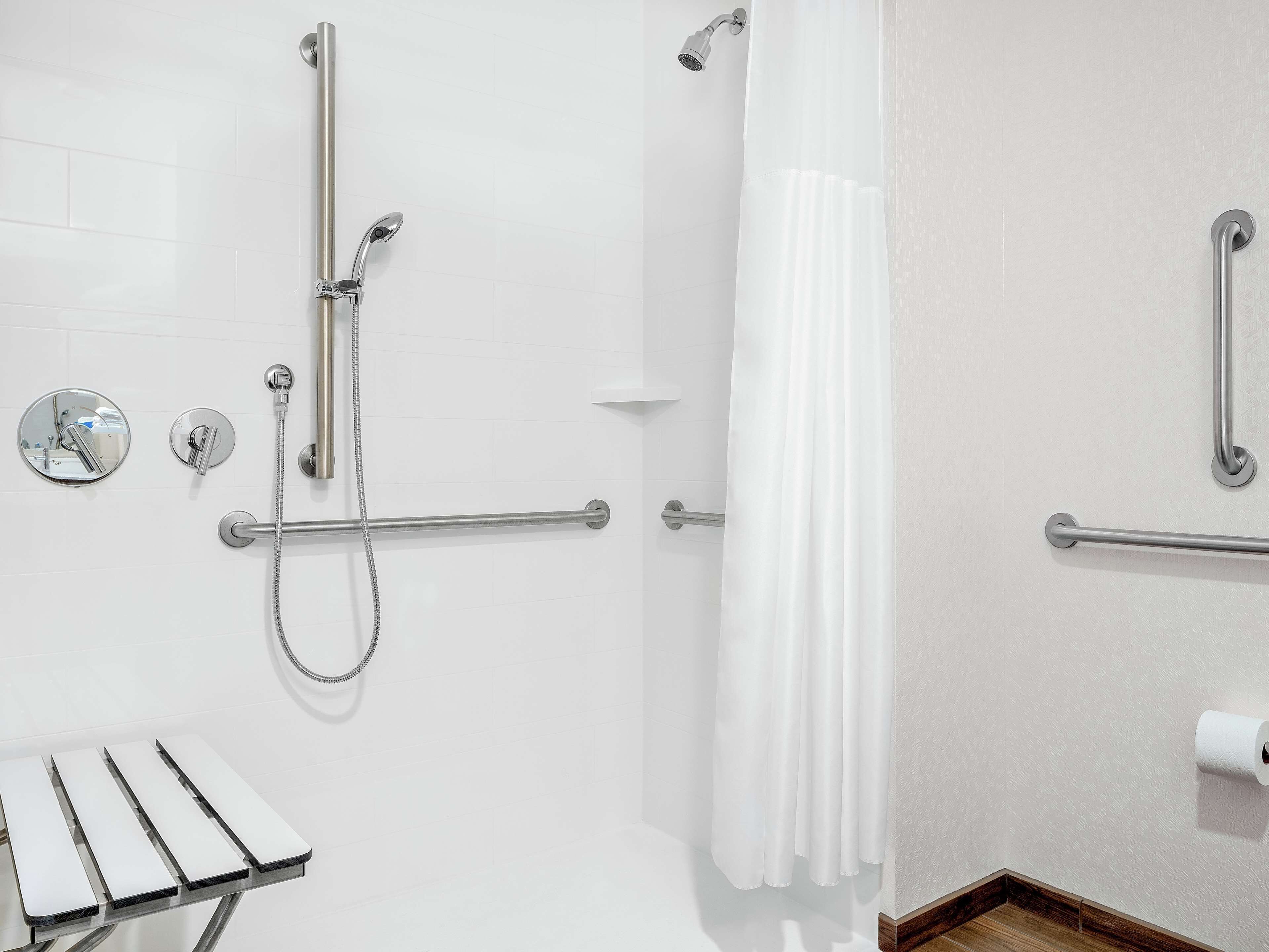 A bathroom with a shower, grab bars, a toilet, and a towel rack.