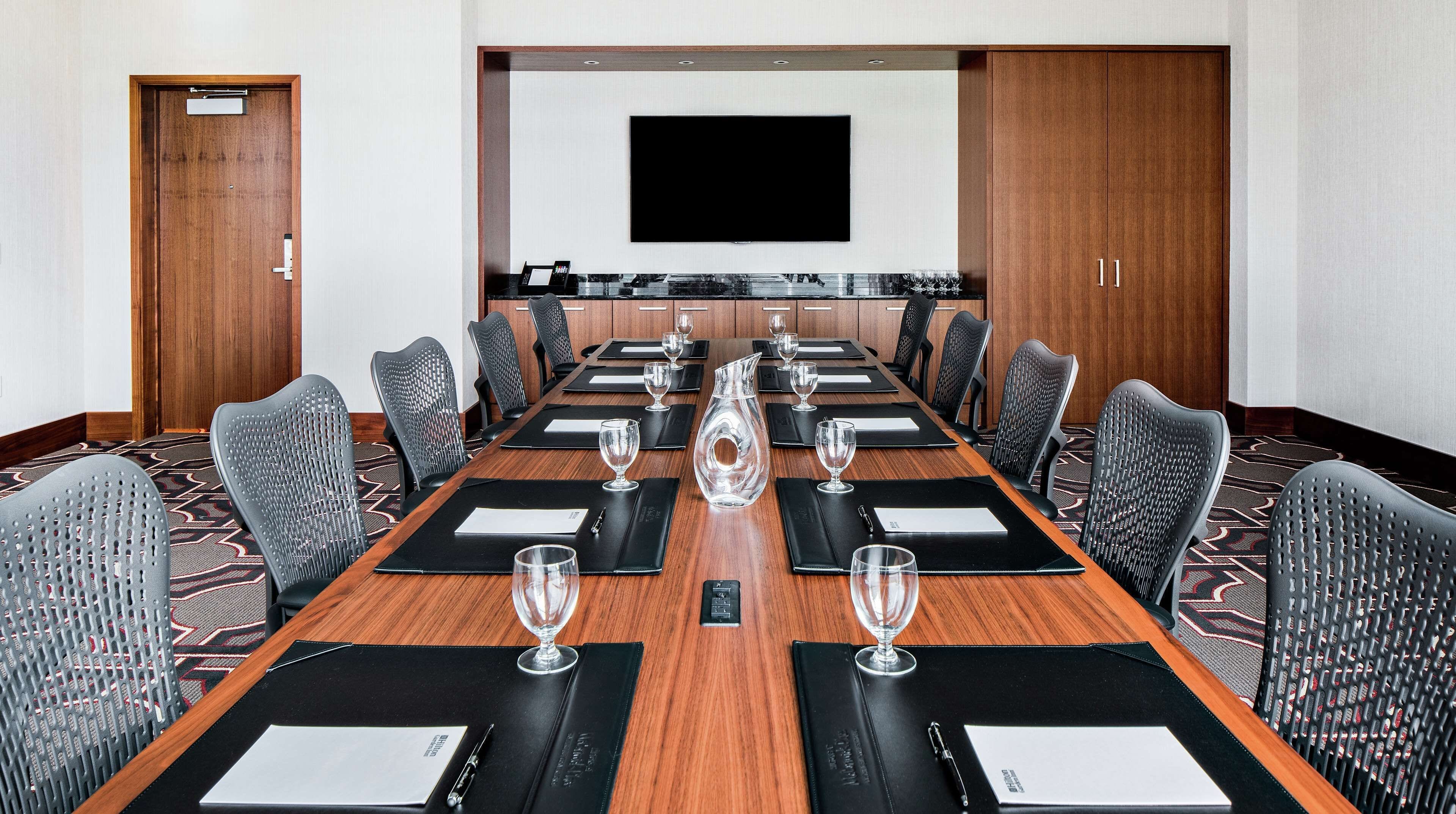 A conference room with a long table, black chairs, and a TV screen on the wall.