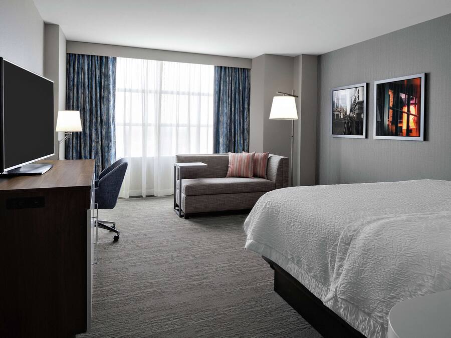 Una habitación de hotel con cama, escritorio con televisor, sofá y sillón.