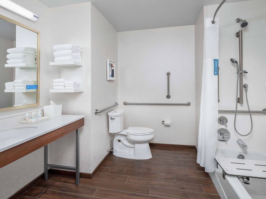 A modern bathroom with a toilet, sink, and shower. It includes grab bars and a towel rack.