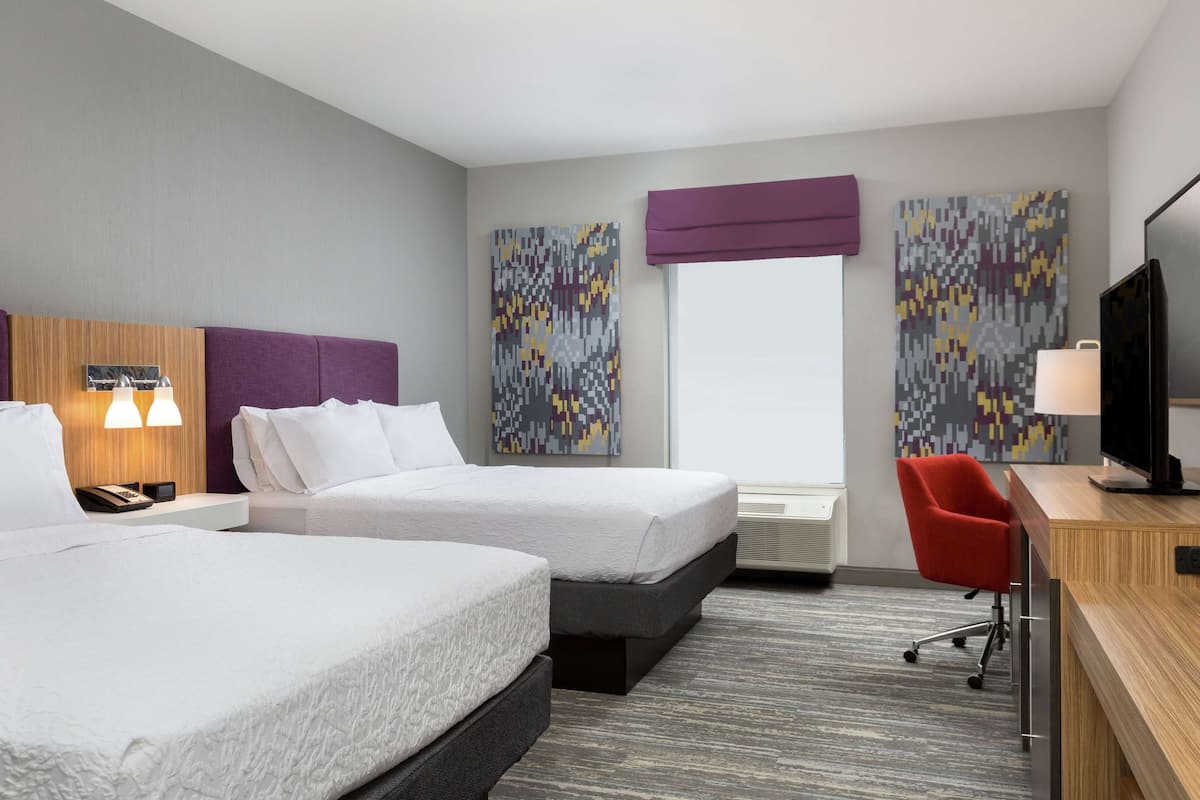 A hotel room with two beds, a desk with a chair, a television, and artwork on the walls.