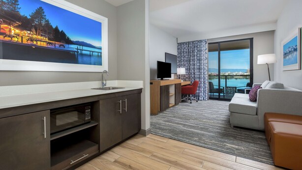Een moderne hotelkamer met een grote televisie, een bureau, een bank en uitzicht op een waterpartij.
