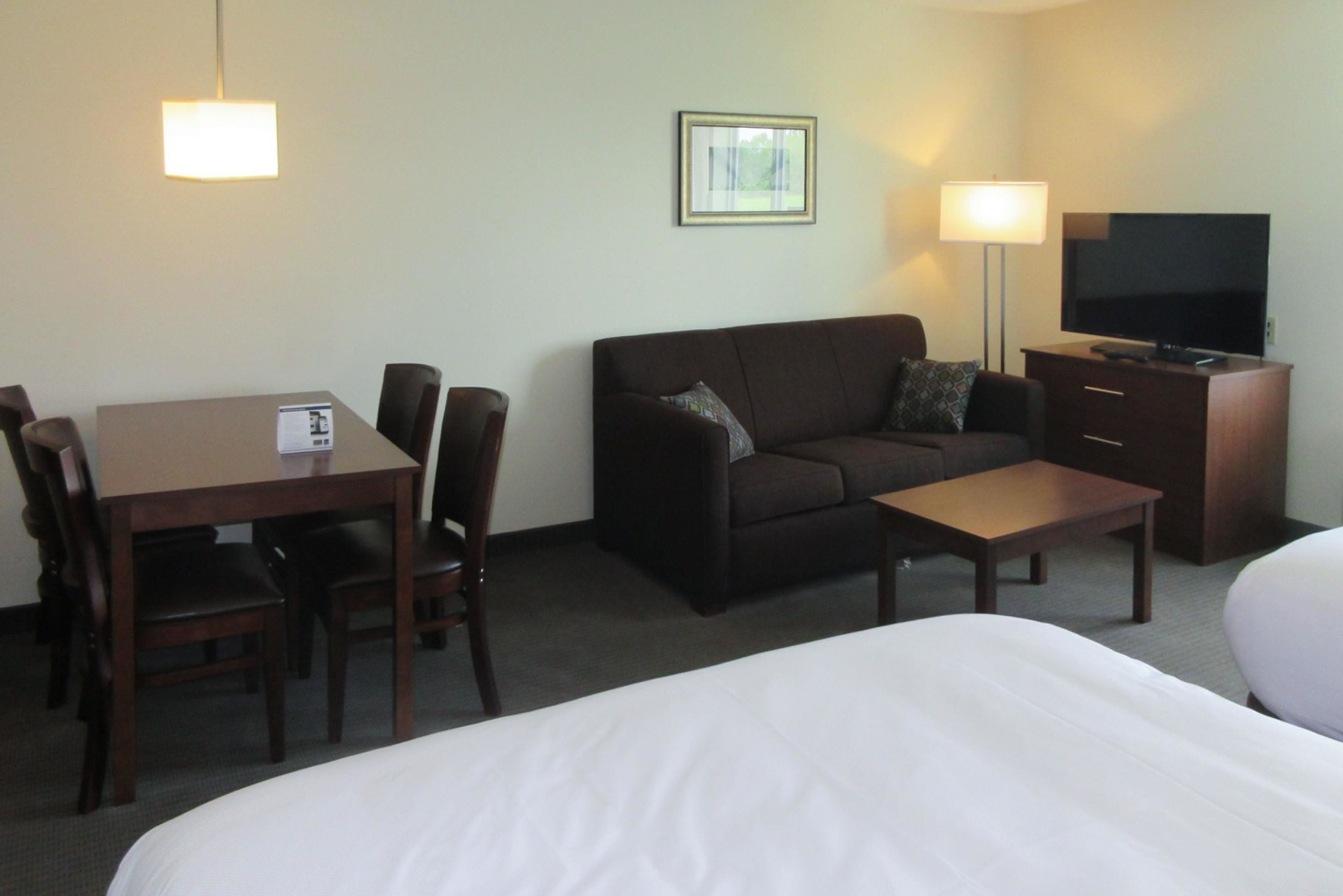 A hotel room with a bed, a sofa, a TV, a desk, and a lamp.
