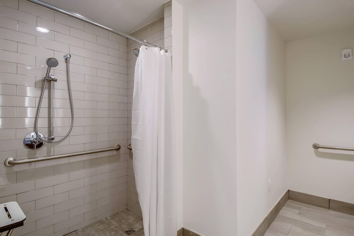 Ducha con cortina blanca, cabezal de ducha de mano y barra de apoyo.