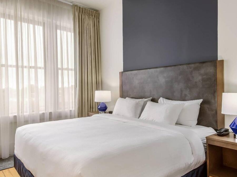 A hotel room with a large bed, a nightstand, a lamp, and a window with curtains.