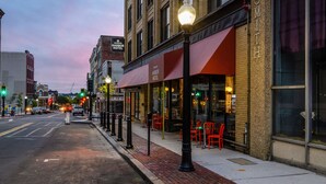 A street view with a hotel named "Harbor Hotel" featuring a red awning and outdoor seating with red chairs.