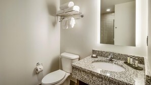 A bathroom with a toilet, a sink with a granite countertop, a towel rack with towels, and a mirror.