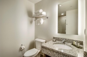 A bathroom with a toilet, a sink with a granite countertop, a towel rack with towels, and a mirror.