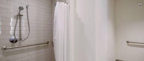 A shower area with a white tiled wall, a showerhead, a curtain, and a handrail.