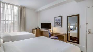 A hotel room with two beds, a desk with a TV, a mirror, and a window with curtains.
