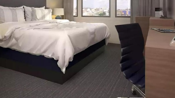 A hotel room with a large bed, a desk, and a view of a cityscape through the window.