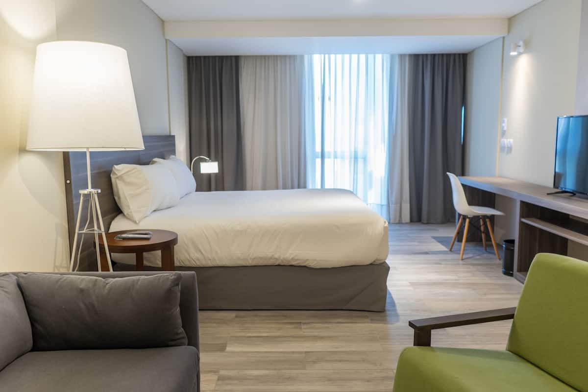 A hotel room with a bed, a desk, a television, a lamp, and a chair.