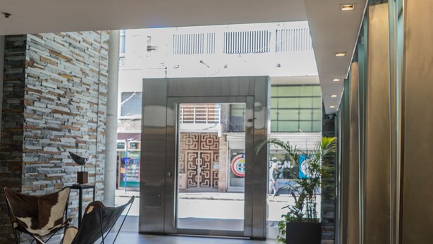A modern lobby with a brick wall, a seating area, and a glass door leading outside. - Olmos Suites (Córdoba)