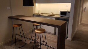 A compact kitchen with a dark countertop, two wooden stools, a microwave, and a hanging light fixture. - Olmos Suites (Córdoba)