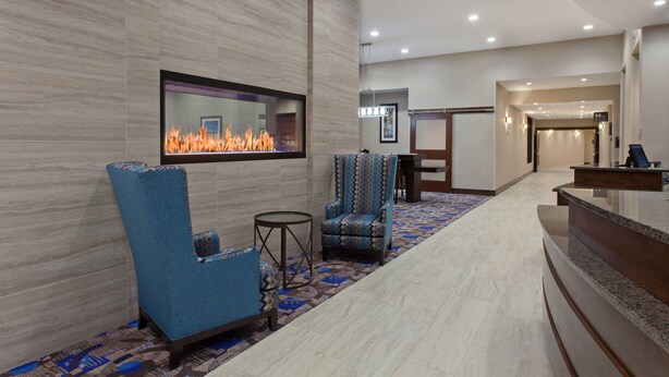 Un hall d’entrée avec une cheminée, des fauteuils bleus, un comptoir d’accueil et une moquette à motifs.