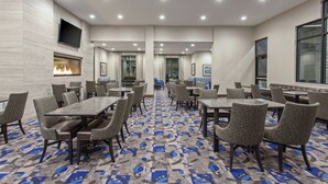 Une salle de conférence d’hôtel avec plusieurs tables et chaises, un téléviseur à écran plat fixé au mur et une moquette à motifs.