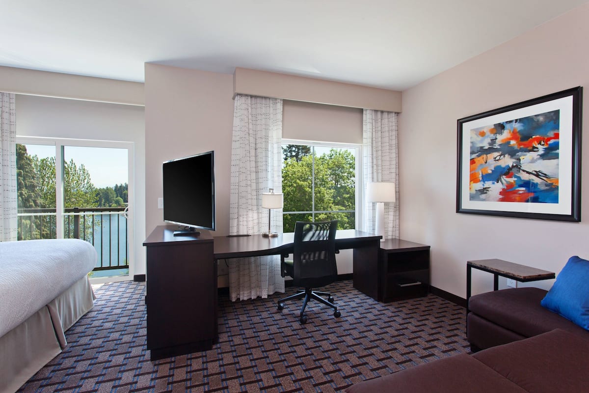 A hotel room with a bed, desk, chair, TV, and a painting on the wall.