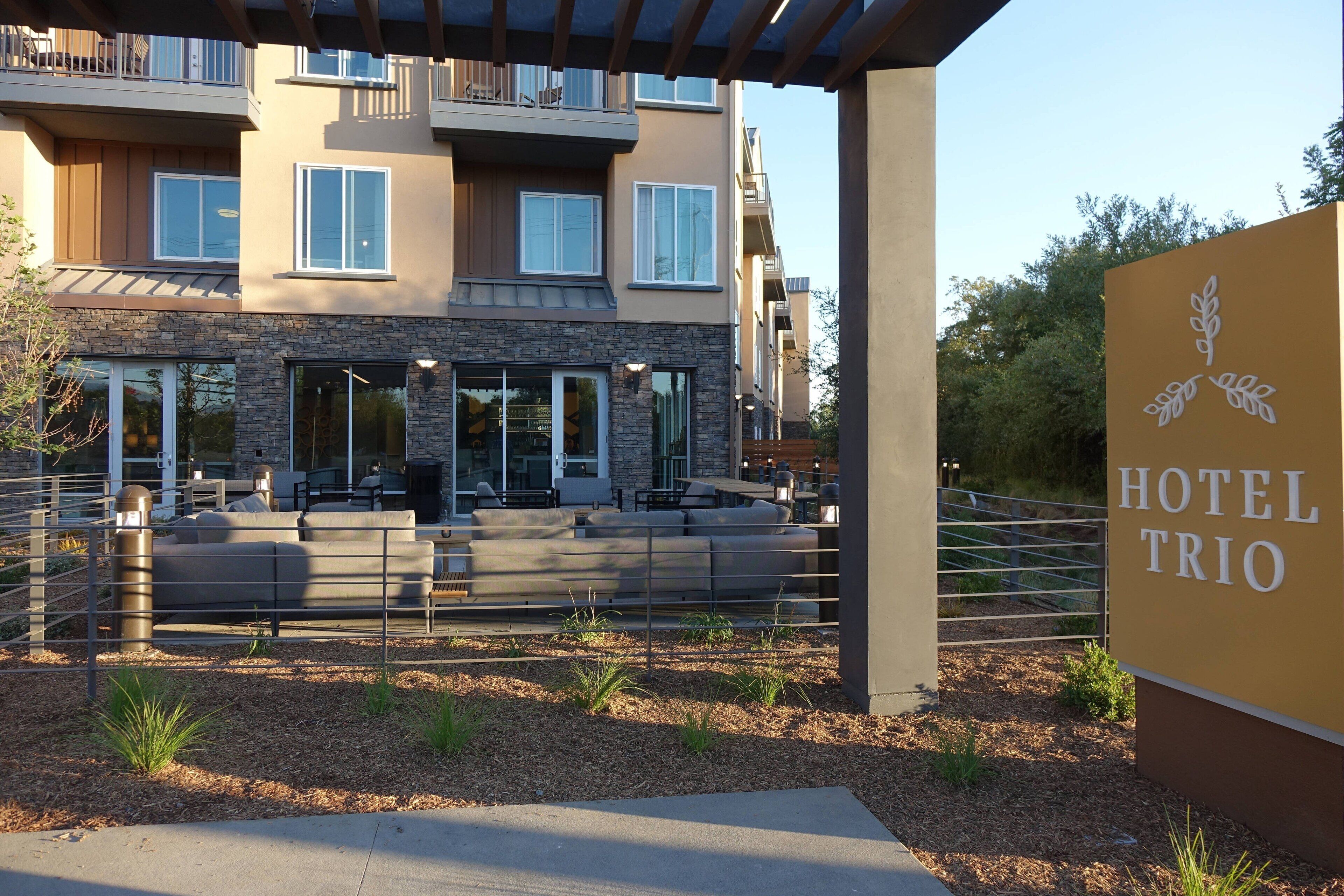 A modern hotel with a stone facade, outdoor seating area, and a sign reading "HOTEL TRIO".