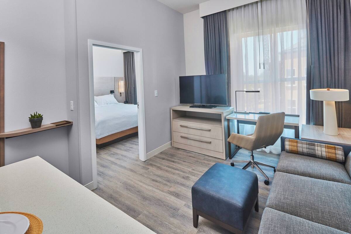 Ein modernes Hotelzimmer mit einem Bett, einem Schreibtisch mit Fernseher, einem Sessel, einer Couch und einer Lampe.