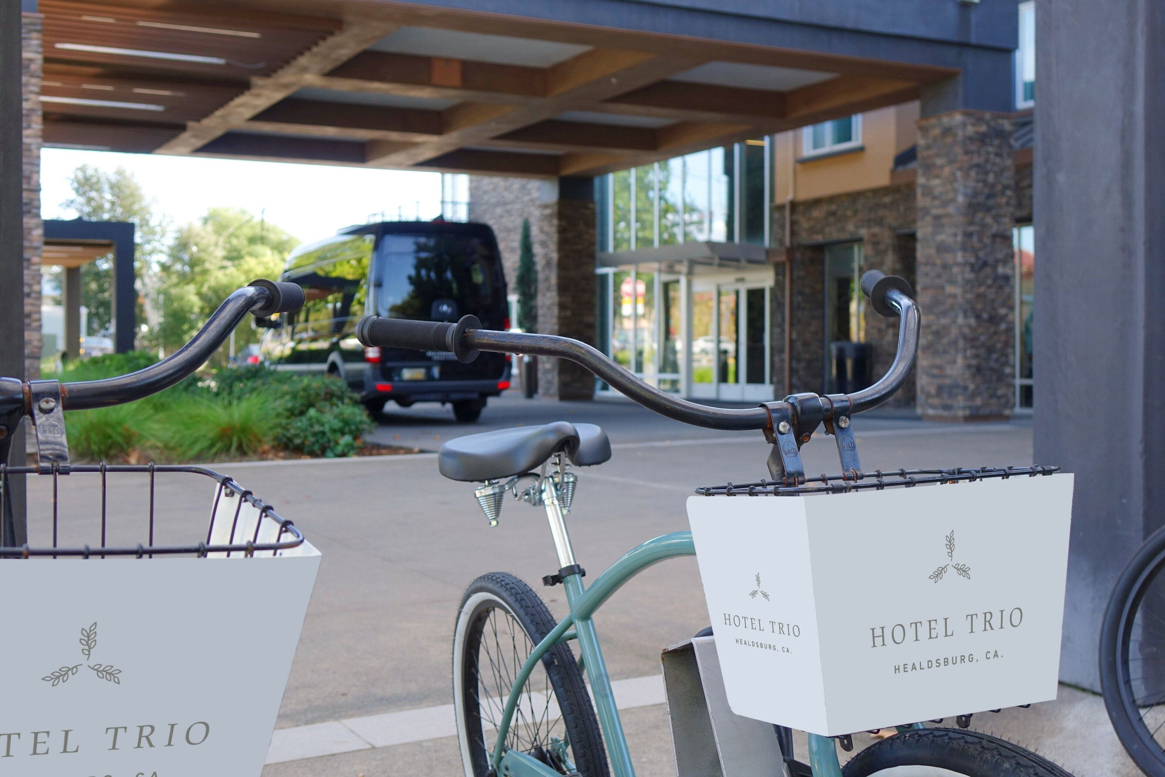 Una bicicleta con canasta y una caja que dice 'Hotel Trio' estacionada frente a un edificio.