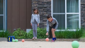 Zwei Kinder spielen mit Bällen in einem Innenhof mit einer Steinmauer und einem Fenster.