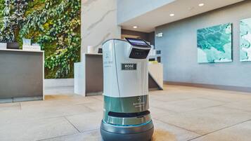 A robotic vacuum cleaner in a hotel lobby with a green wall and artwork.