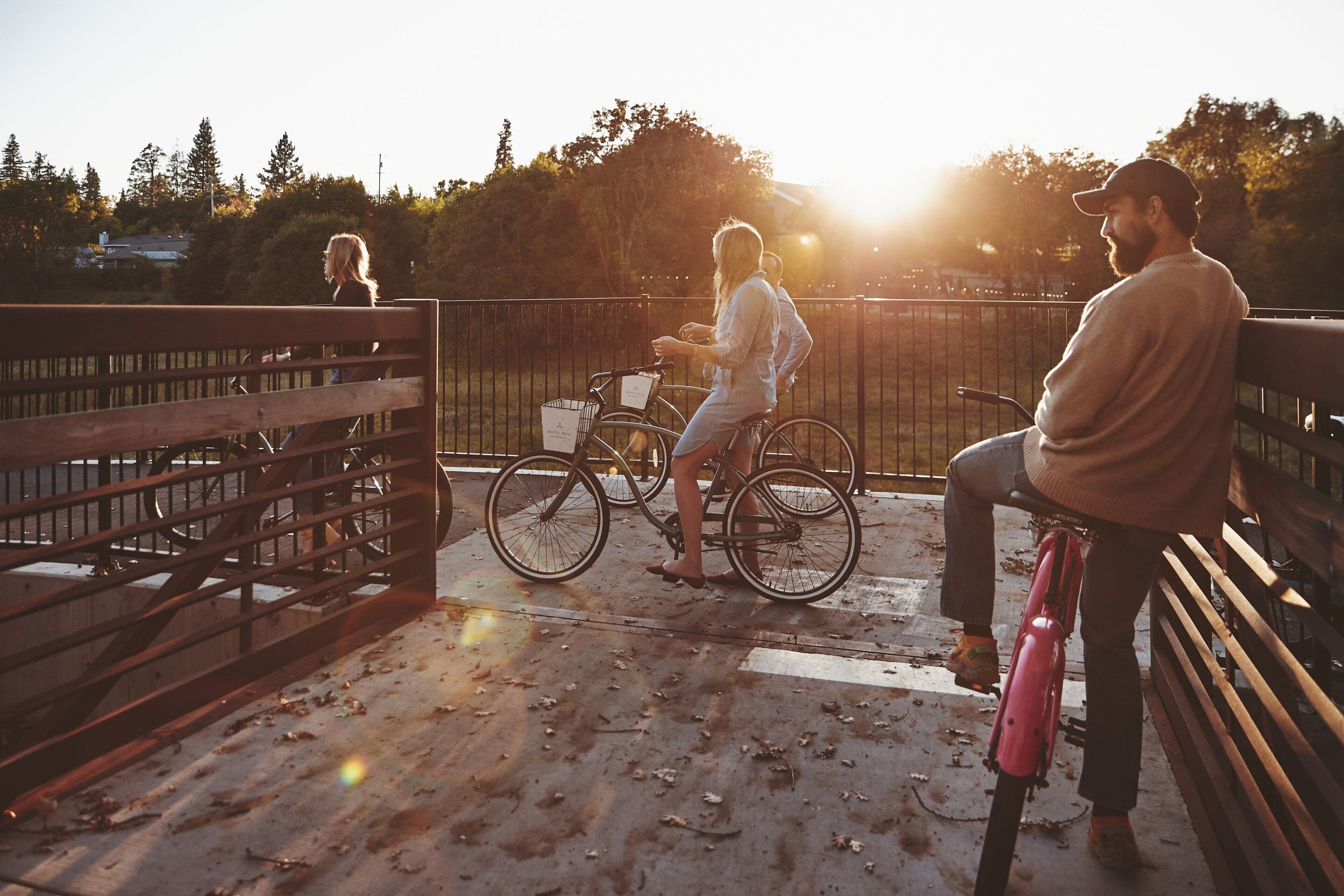 A person sitting on a bench, another person standing next to a bicycle, and a third person walking away.