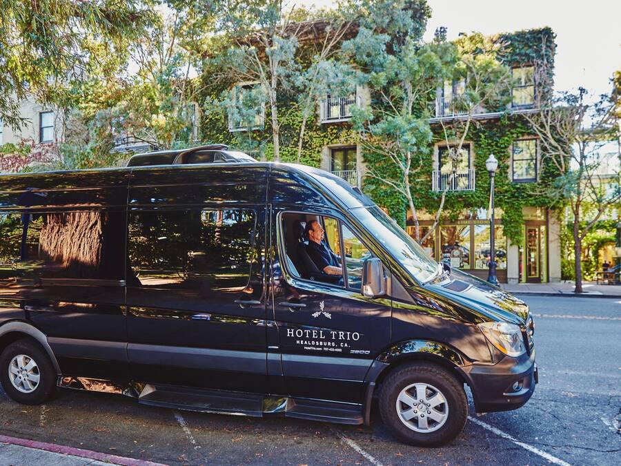 A black van with "HOTEL TRIO" and "HEALDSBURG, CA." on the side, parked on a street with trees and buildings in the background.