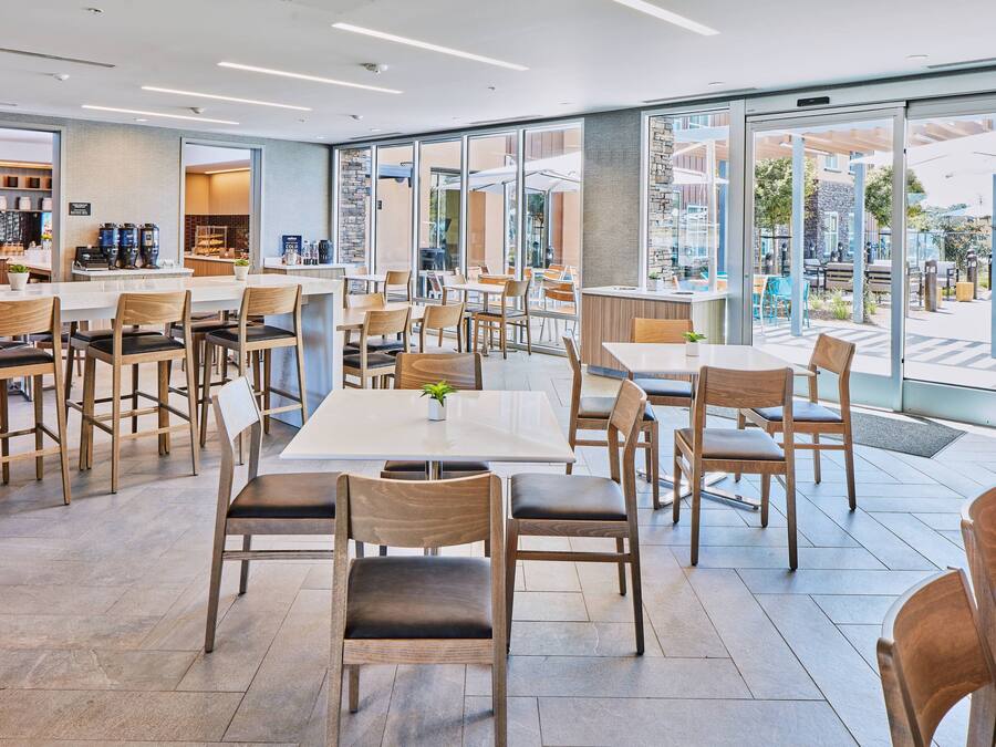 Un café moderno con sillas y mesas de madera, ventanas amplias y vistas al exterior.