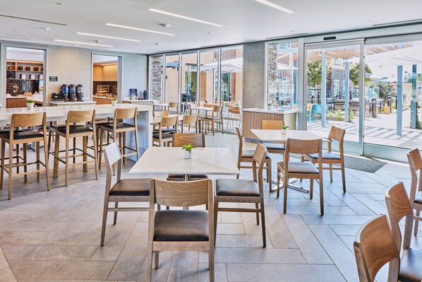 A modern cafe with wooden chairs and tables, large windows, and a view of the outdoors.