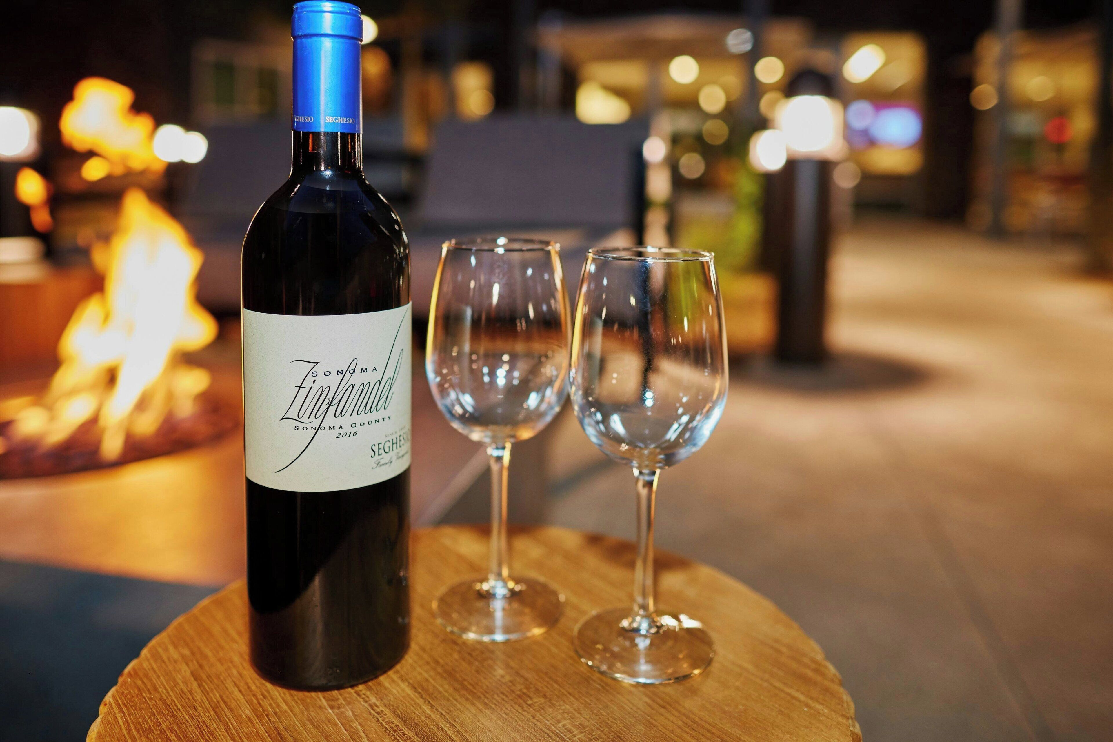 A bottle of wine and two glasses on a wooden table with a blurred background.