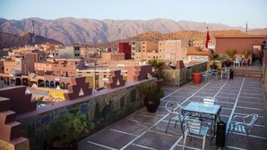 Una terraza en la azotea con mobiliario exterior, plantas en macetas y vistas a un paisaje montañoso.