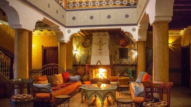 Un interior tradicional marroquí con una zona de estar central, columnas ornamentales y una chimenea decorativa.